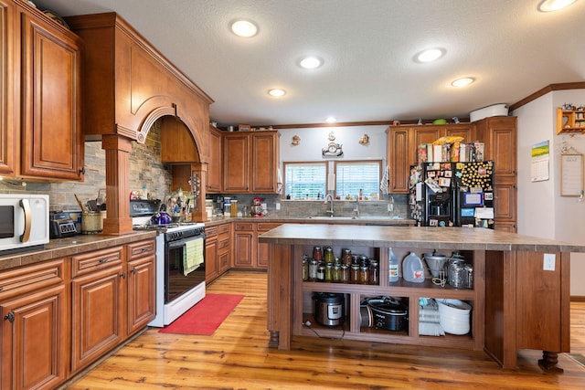 kitchen with light hardwood / wood-style flooring, ornamental molding, white appliances, and a kitchen island