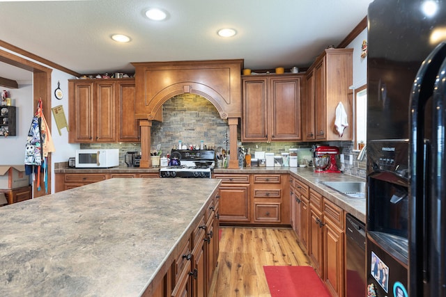 kitchen with black appliances, tasteful backsplash, premium range hood, crown molding, and light hardwood / wood-style flooring