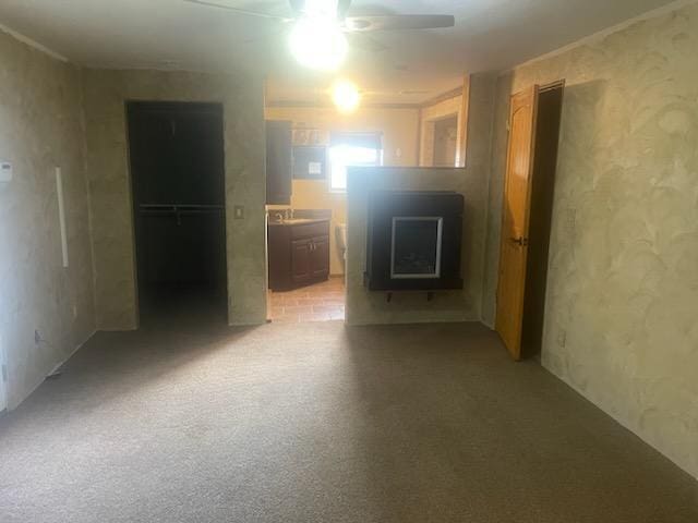 carpeted spare room featuring a wood stove and ceiling fan