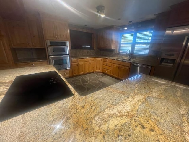 kitchen featuring light stone countertops, decorative backsplash, stainless steel appliances, and sink