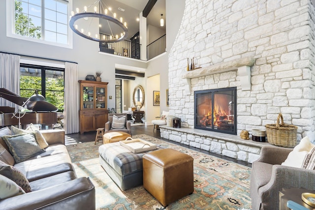 living room featuring wood-type flooring, a stone fireplace, an inviting chandelier, and a high ceiling