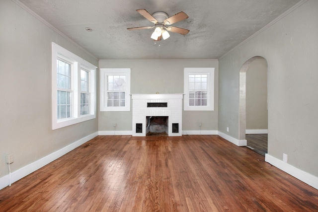 unfurnished living room featuring a healthy amount of sunlight, crown molding, a fireplace, and dark hardwood / wood-style floors