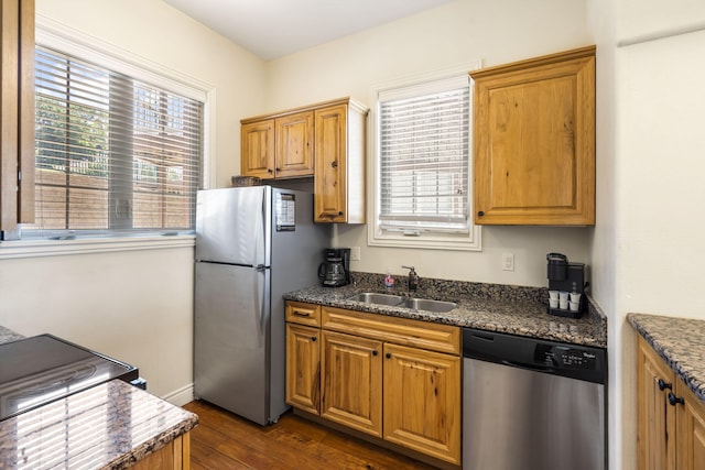 kitchen with appliances with stainless steel finishes, dark stone counters, sink, and dark hardwood / wood-style floors