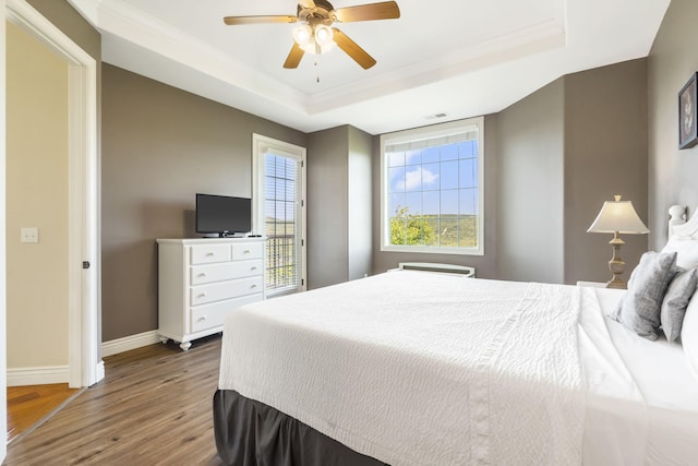 bedroom featuring ornamental molding, ceiling fan, a tray ceiling, and wood-type flooring