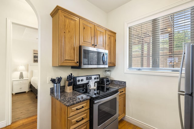 kitchen featuring stainless steel appliances, dark stone counters, and light hardwood / wood-style flooring