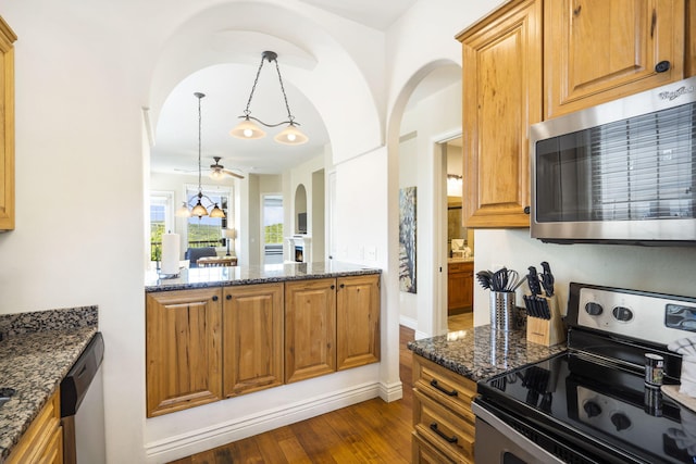 kitchen with stainless steel appliances, dark stone counters, dark wood-type flooring, and decorative light fixtures