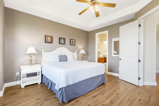 bedroom featuring ceiling fan, ensuite bath, a tray ceiling, and light hardwood / wood-style flooring