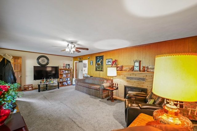 carpeted living room with ceiling fan, a fireplace, wood walls, and ornamental molding