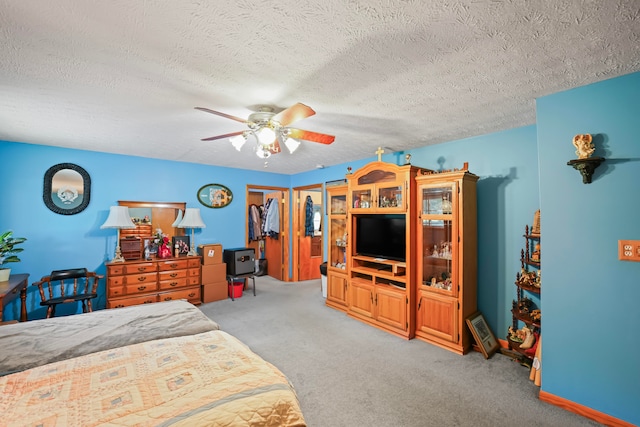 bedroom featuring a walk in closet, ceiling fan, light carpet, a closet, and a textured ceiling