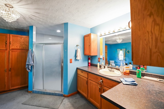 bathroom featuring an inviting chandelier, a shower with shower door, vanity, and a textured ceiling