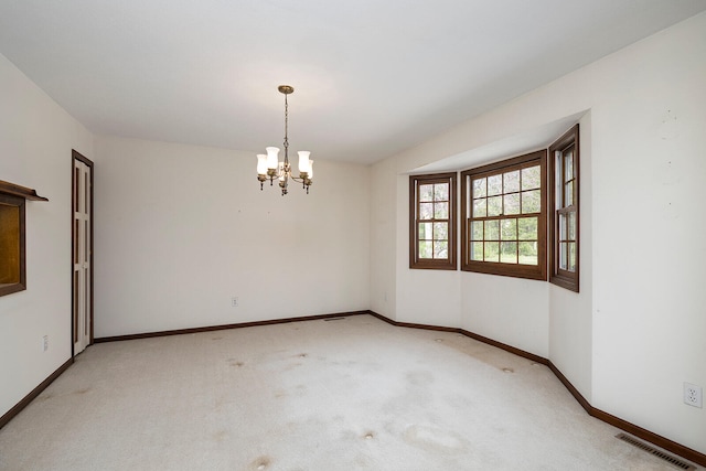 empty room featuring light colored carpet and a notable chandelier