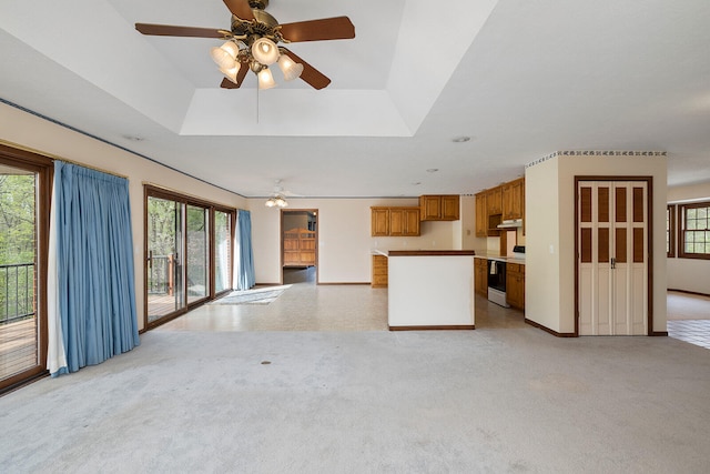 unfurnished living room with a raised ceiling, light carpet, and ceiling fan