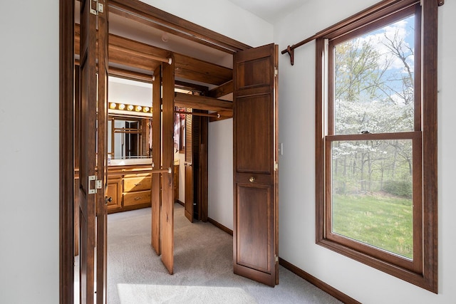 corridor featuring baseboards, light carpet, and a wealth of natural light