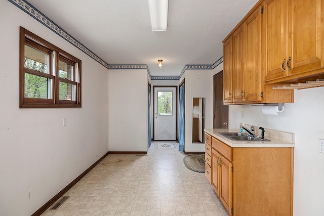 kitchen featuring a sink, brown cabinets, light countertops, baseboards, and visible vents