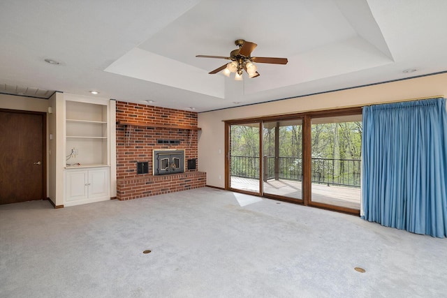 unfurnished living room featuring ceiling fan, built in features, a tray ceiling, light colored carpet, and a brick fireplace