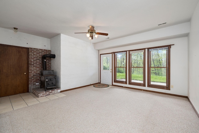 unfurnished living room with a wood stove, ceiling fan, and light colored carpet