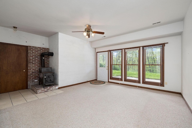 unfurnished living room featuring a wood stove, ceiling fan, a wealth of natural light, and carpet flooring