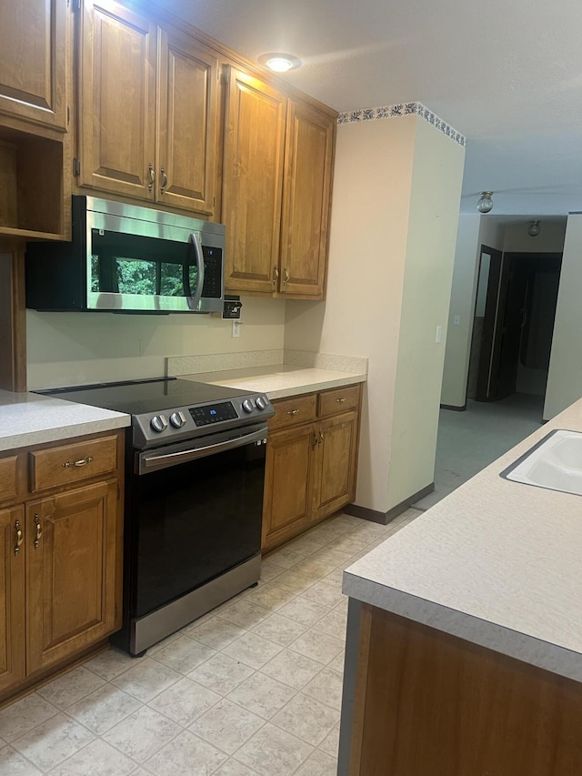 kitchen featuring brown cabinetry, appliances with stainless steel finishes, a sink, and light countertops