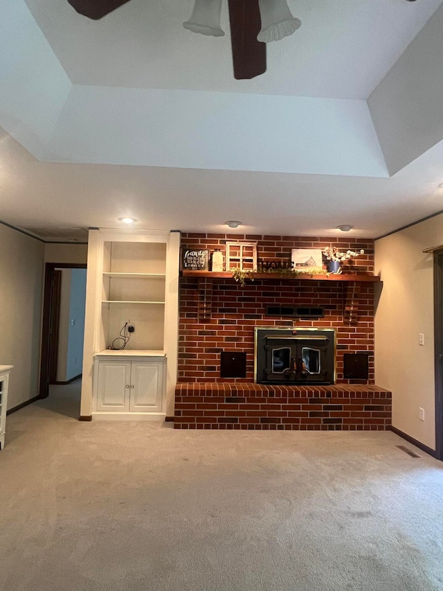 unfurnished living room with a fireplace, built in shelves, carpet floors, and a raised ceiling