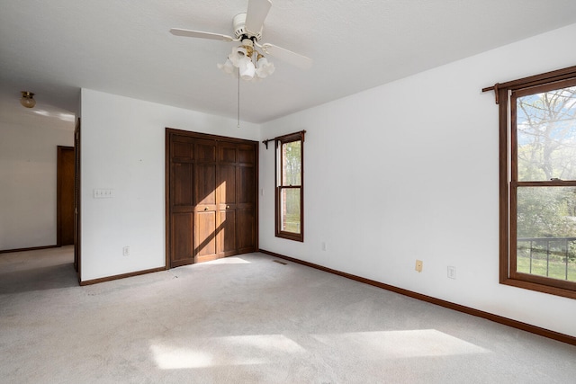 unfurnished bedroom featuring light carpet, multiple windows, a closet, and ceiling fan