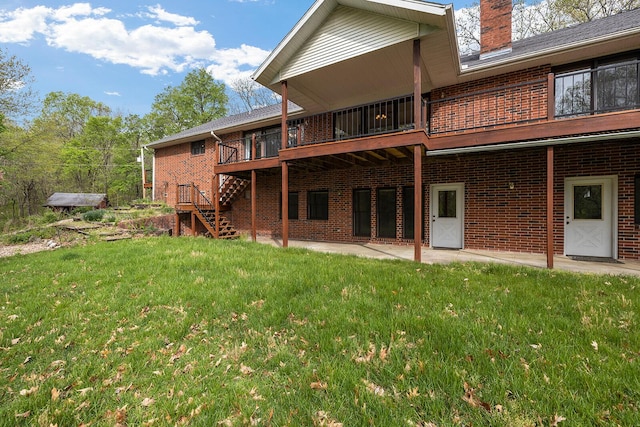 back of property featuring a chimney, stairs, a wooden deck, a lawn, and brick siding