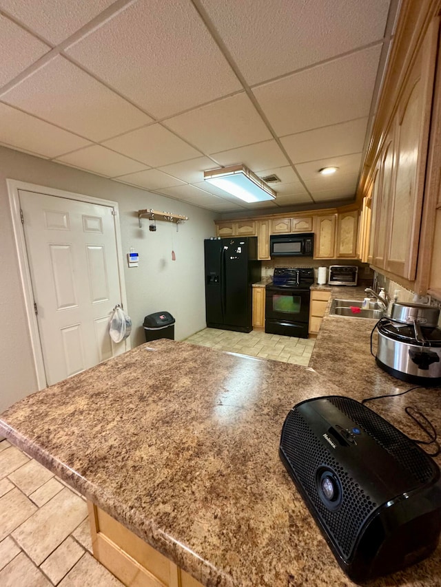 kitchen featuring light tile patterned flooring, a drop ceiling, black appliances, and sink