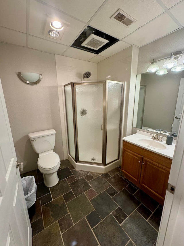 bathroom with toilet, a drop ceiling, vanity, and walk in shower