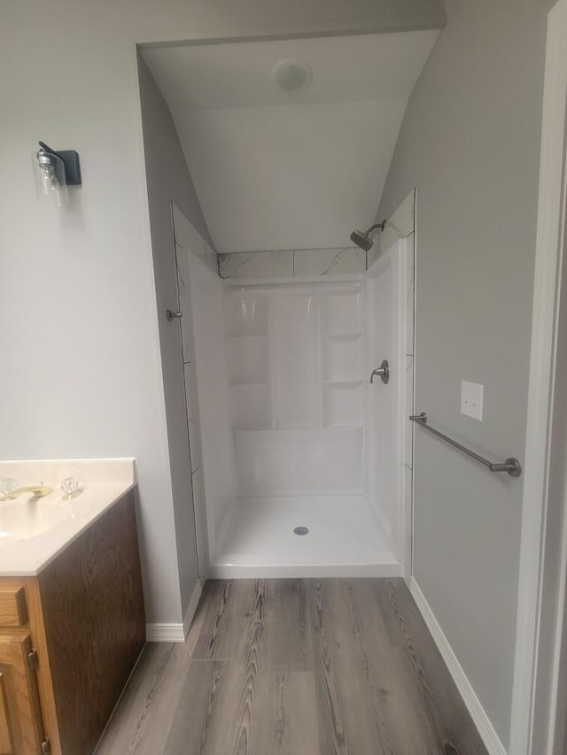 bathroom featuring wood-type flooring, vanity, vaulted ceiling, and a shower