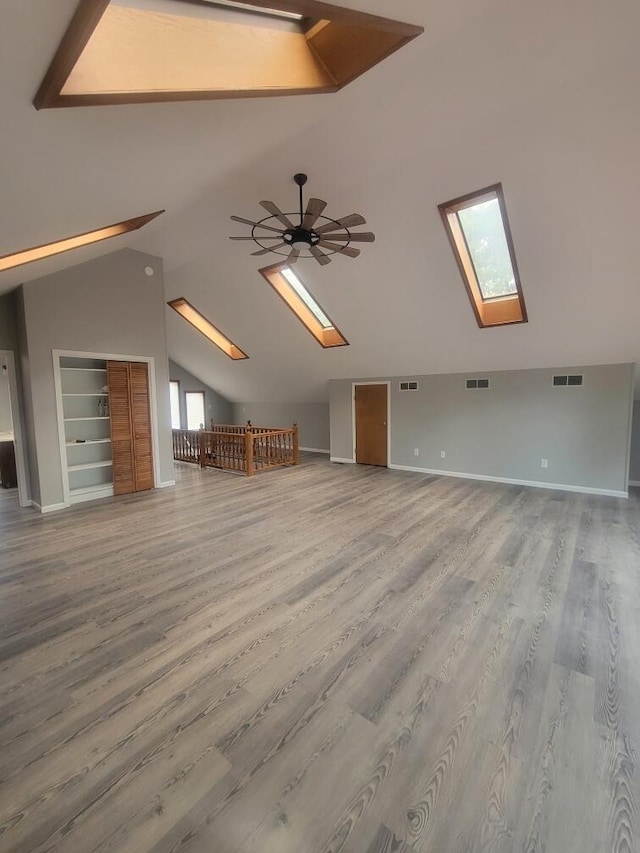 bonus room featuring ceiling fan, hardwood / wood-style flooring, vaulted ceiling with skylight, and built in shelves