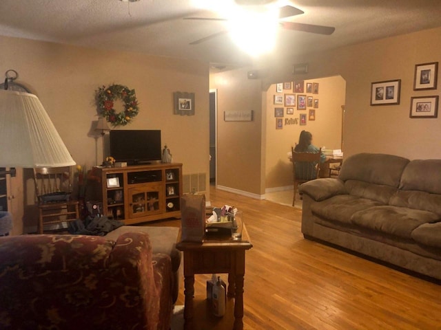 living room featuring light hardwood / wood-style flooring, a textured ceiling, and ceiling fan