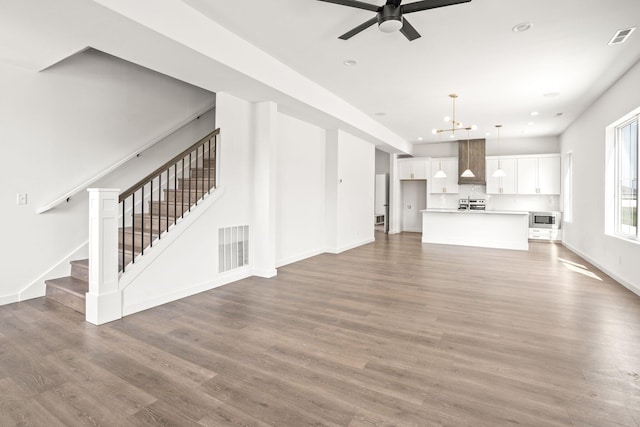 unfurnished living room featuring ceiling fan with notable chandelier and wood-type flooring