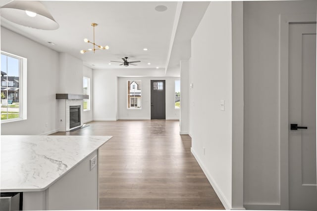 kitchen with wood-type flooring, ceiling fan with notable chandelier, decorative light fixtures, and light stone counters