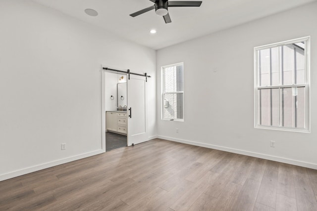 unfurnished bedroom with ceiling fan, a barn door, connected bathroom, and light hardwood / wood-style floors