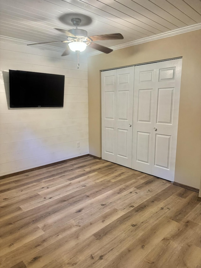 unfurnished bedroom with wood finished floors, a ceiling fan, a closet, crown molding, and baseboards