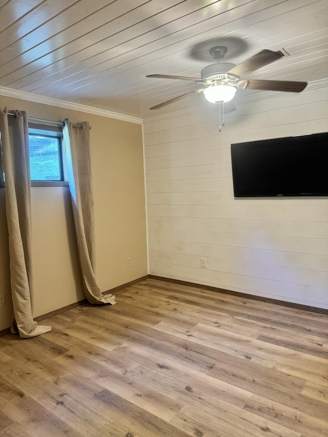 empty room with a ceiling fan, crown molding, wood walls, light wood-type flooring, and baseboards