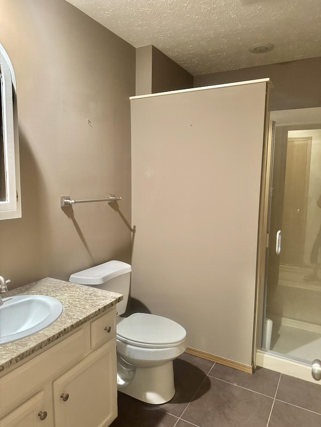 bathroom featuring a shower stall, a textured ceiling, vanity, toilet, and tile patterned flooring