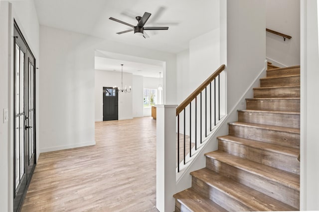 stairway featuring ceiling fan with notable chandelier and wood-type flooring