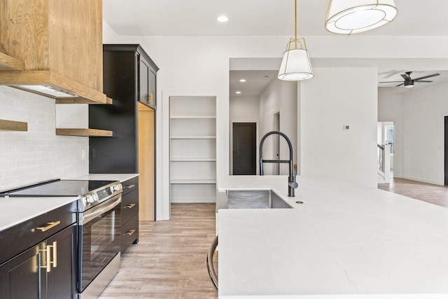 kitchen featuring tasteful backsplash, sink, stainless steel electric range oven, light hardwood / wood-style floors, and decorative light fixtures