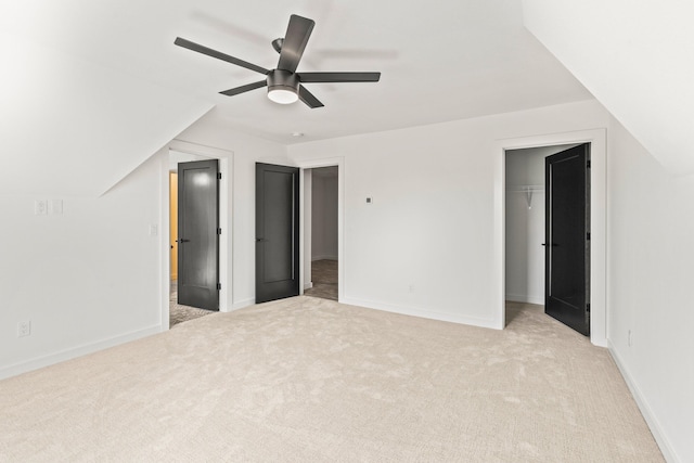 unfurnished bedroom featuring a spacious closet, a closet, light colored carpet, and ceiling fan