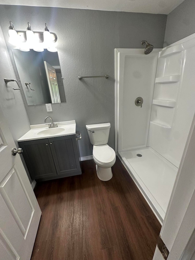 bathroom with walk in shower, vanity, hardwood / wood-style floors, and toilet