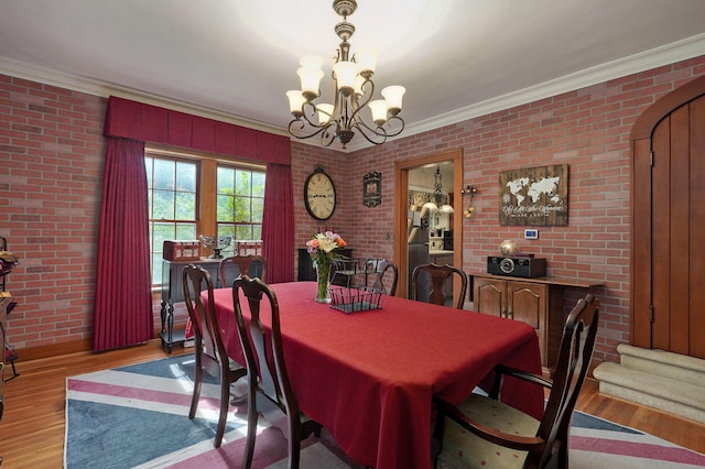 dining area featuring brick wall, light hardwood / wood-style flooring, crown molding, and a notable chandelier