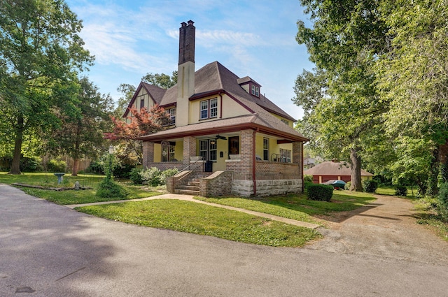 english style home with a porch, a chimney, stucco siding, brick siding, and a front lawn