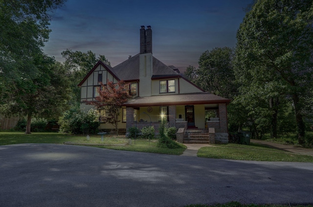 english style home featuring covered porch and a yard