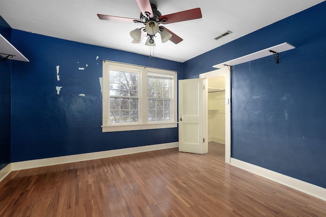 unfurnished bedroom with hardwood / wood-style floors, a walk in closet, and ceiling fan