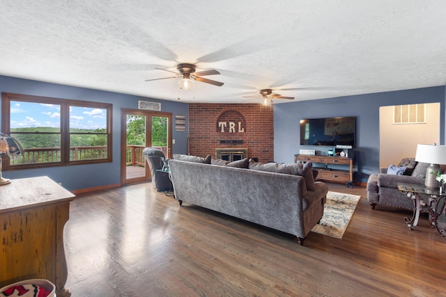 living room with dark wood-type flooring, baseboards, a fireplace, a textured ceiling, and ceiling fan