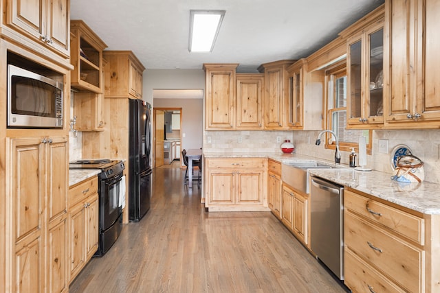 kitchen featuring light stone counters, black appliances, light brown cabinets, tasteful backsplash, and light hardwood / wood-style flooring