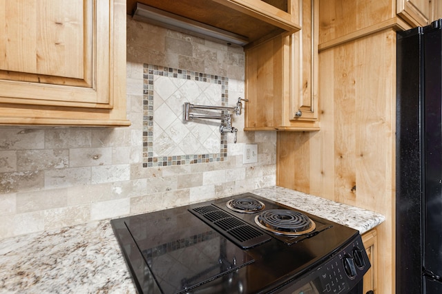 kitchen featuring light brown cabinets, range, backsplash, light stone countertops, and freestanding refrigerator