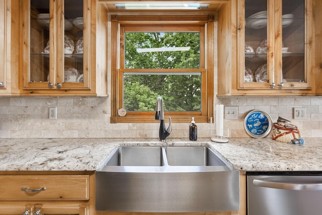 kitchen with stainless steel dishwasher, a sink, backsplash, glass insert cabinets, and light stone countertops