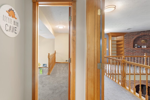 hall featuring carpet, a textured ceiling, baseboards, and an upstairs landing