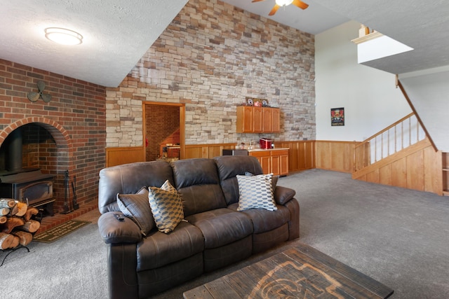 living area with a wood stove, carpet floors, wainscoting, a textured ceiling, and ceiling fan